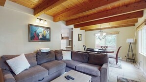 Een woonkamer met een modulaire bank, een salontafel, een schilderij aan de muur en een eetgedeelte met een kroonluchter.