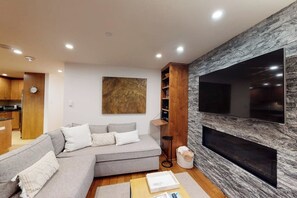 Ein modernes Wohnzimmer mit einem Ecksofa, einem flachbildfernseher an einer Steinwand und einer Holzregaleinheit.