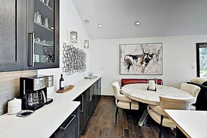 Eine moderne Küche mit Kaffeemaschine, einem Essbereich mit rundem Tisch und Stühlen sowie einem großen abstrakten Gemälde an der Wand.