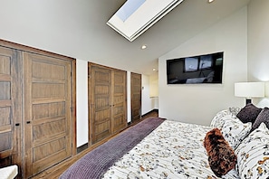 Ein Schlafzimmer mit Oberlicht, Holzschränken, einem Bett mit floralem Bettbezug und einem an der Wand montierten Fernseher.