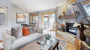Una sala de estar con sofá, mesa de centro, chimenea y un comedor con sillas y una mesa.