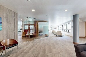 Eine großzügige Lobby mit modernem Design, mit Glastrennwand, einer Sitzecke inklusive Sofas und Sesseln sowie einer großen Säule.