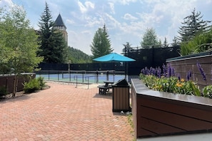 Eine Terrasse mit Pool, einer Holzbank und einem Tisch unter einem blauen Sonnenschirm.