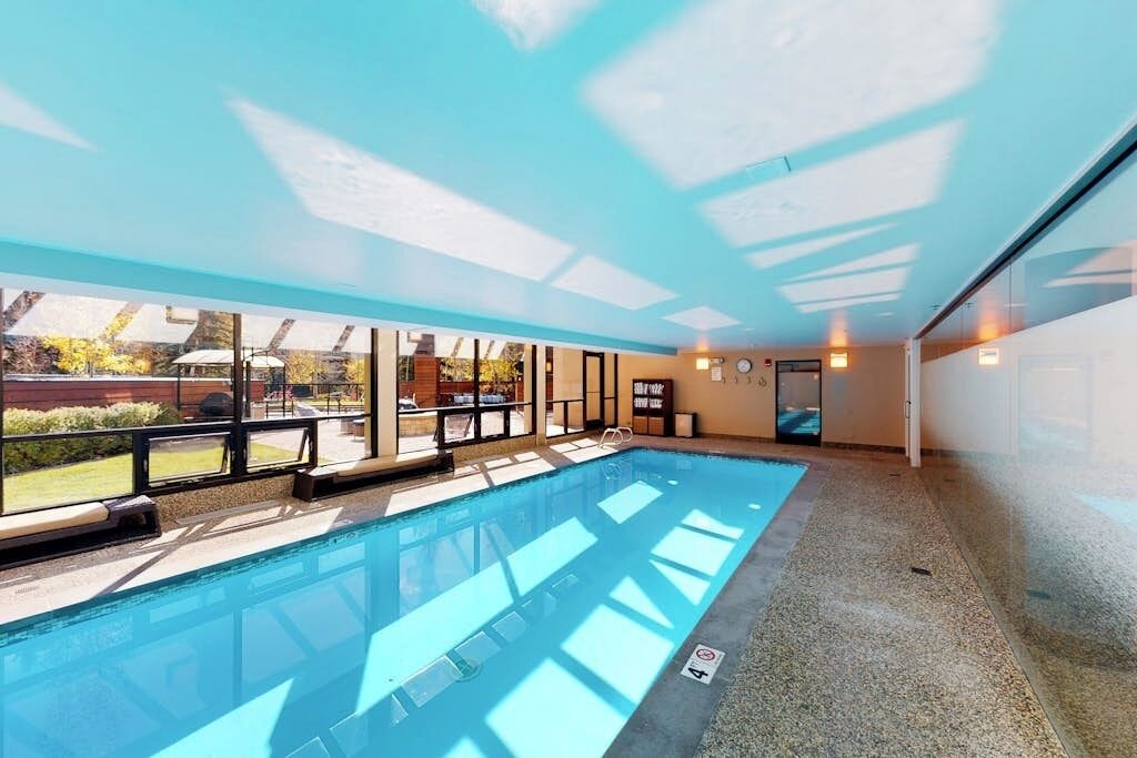 Ein Swimmingpool mit klaren Glaswänden, Blick ins Freie und einer Decke mit Dachfenstern.