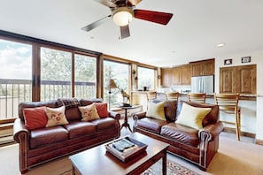Ein geräumiges Wohnzimmer mit großem Fenster, Deckenventilator und Küchenzeile mit Holzschränken.