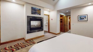 A hotel room with a bed, a fireplace, a hallway, and a door leading to a bathroom. - Huge Multi-Level Home with Hot Tub, Separate Studio Apartment & Vail Views (Vail)