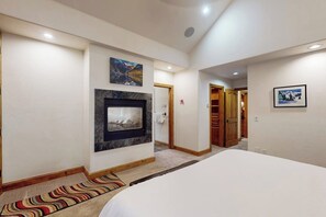 A hotel room with a bed, a fireplace, a hallway, and a door leading to a bathroom. - Huge Multi-Level Home with Hot Tub, Separate Studio Apartment & Vail Views (Vail)