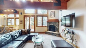 A living room with a stone fireplace, leather sofa, glass coffee table, and a television mounted on the wall. - Huge Multi-Level Home with Hot Tub, Separate Studio Apartment & Vail Views (Vail)