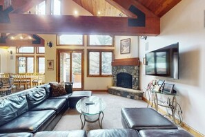 A living room with a stone fireplace, leather sofa, glass coffee table, and a television mounted on the wall. - Huge Multi-Level Home with Hot Tub, Separate Studio Apartment & Vail Views (Vail)