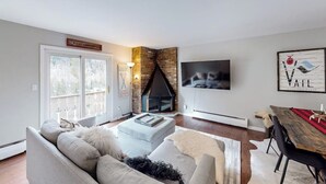 Een woonkamer met een open haard, een bank, een eettafel en een televisie aan de muur.