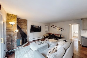 A living room with a fireplace, a sofa, a TV, and a dining area. - Mountain Views at Vail East | Fireplace, Desk, Walk to Vail Shuttle & Trails (Vail)
