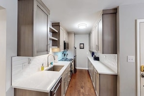 A narrow kitchen with white countertops, stainless steel appliances, and wooden cabinets. - Mountain Views at Vail East | Fireplace, Desk, Walk to Vail Shuttle & Trails (Vail)