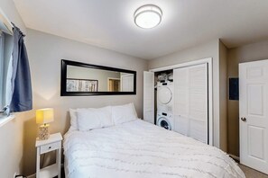 A bedroom with a bed, a nightstand with a lamp, a mirror, a wardrobe, and a washing machine. - Mountain Views at Vail East | Fireplace, Desk, Walk to Vail Shuttle & Trails (Vail)
