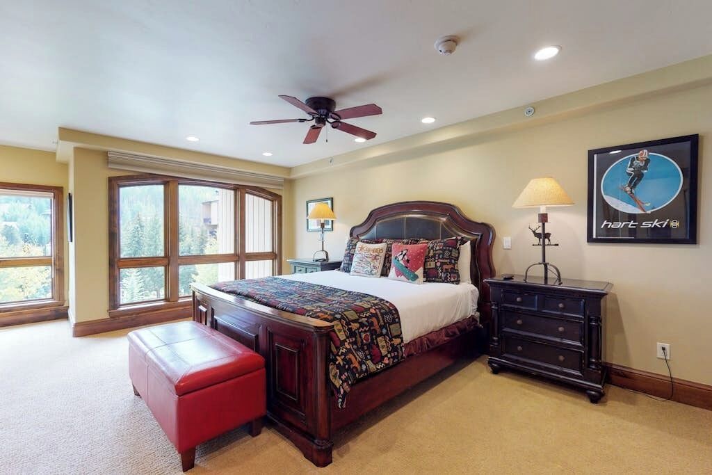 A bedroom with a large bed, a ceiling fan, a dresser, and a window with a view.