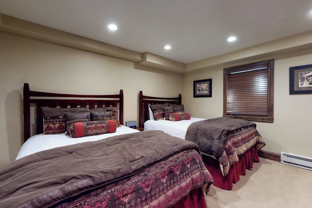 A bedroom with two beds, a window with blinds, and a framed picture on the wall.