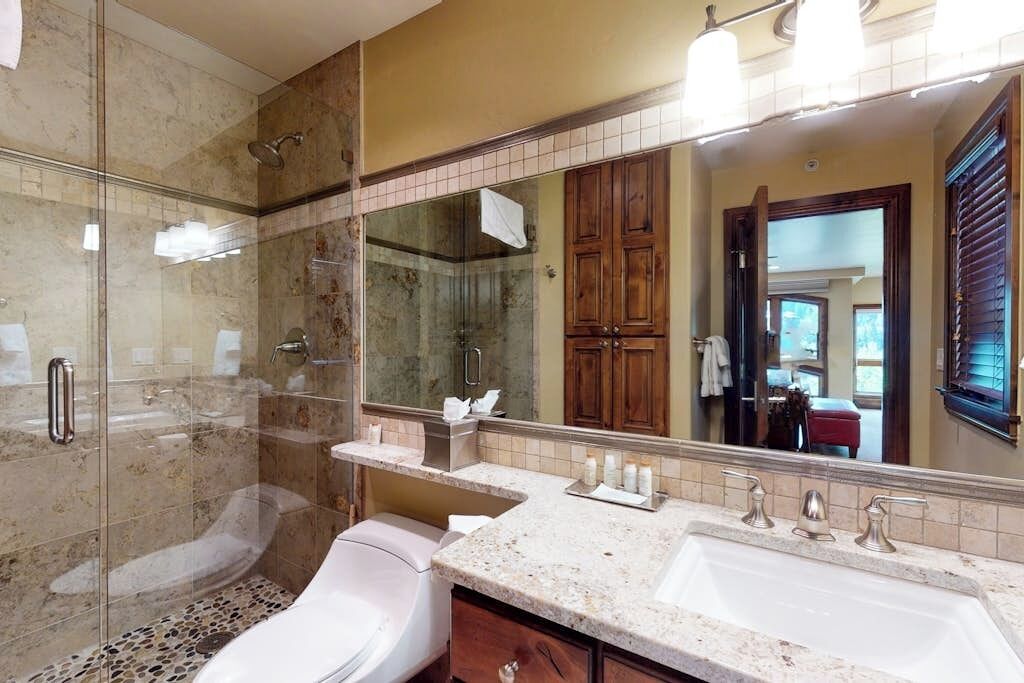 Une salle de bain avec une douche à parois de verre, des toilettes blanches, un meuble-lavabo et un grand miroir.