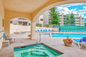An outdoor swimming pool area with lounge chairs, a hot tub, and a view of a residential building. - Ground Floor Mountain Condo with Shared Pool & Hot Tub - Free Ski Shuttle (Avon)