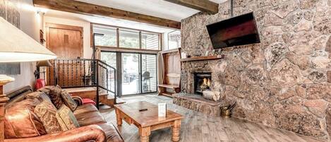 A cozy living room with a stone fireplace, leather sofa, and a wooden coffee table.