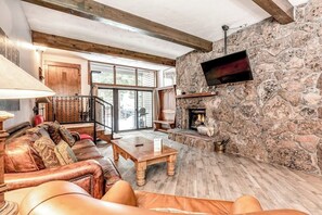 A cozy living room with a stone fireplace, leather sofa, and a wooden coffee table. - Ground Floor Mountain Condo with Shared Pool & Hot Tub - Free Ski Shuttle (Avon)