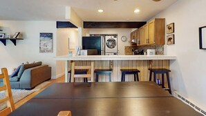 Uma cozinha compacta com máquina de lavar e secar integradas, armários de madeira e um espaço de jantar com mesa e cadeiras.