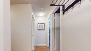 Um corredor estreito com piso de madeira, paredes brancas e um quadro pendurado na parede.