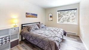 Un dormitorio con cama, mesita de noche, lámpara, ventana con vistas y estante con cajones.