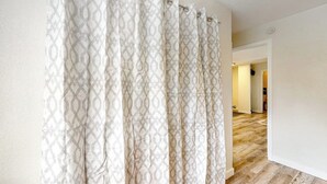 Un pasillo con una cortina estampada, suelo de madera y un acceso a otra habitación.
