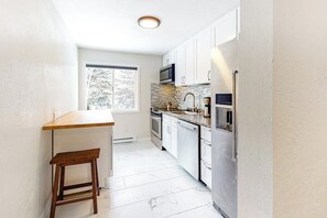 A kitchen with white cabinets, a stainless steel refrigerator, a microwave, a stove, and a window with a view of trees. - Remodeled mountain view condo with free WiFi and easy access to slopes (Avon)