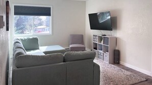 Una sala de estar con un sofá, una silla, un televisor y una estantería.