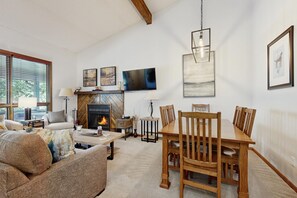 Una sala de estar con chimenea, una mesa de comedor y un televisor montado en la pared.