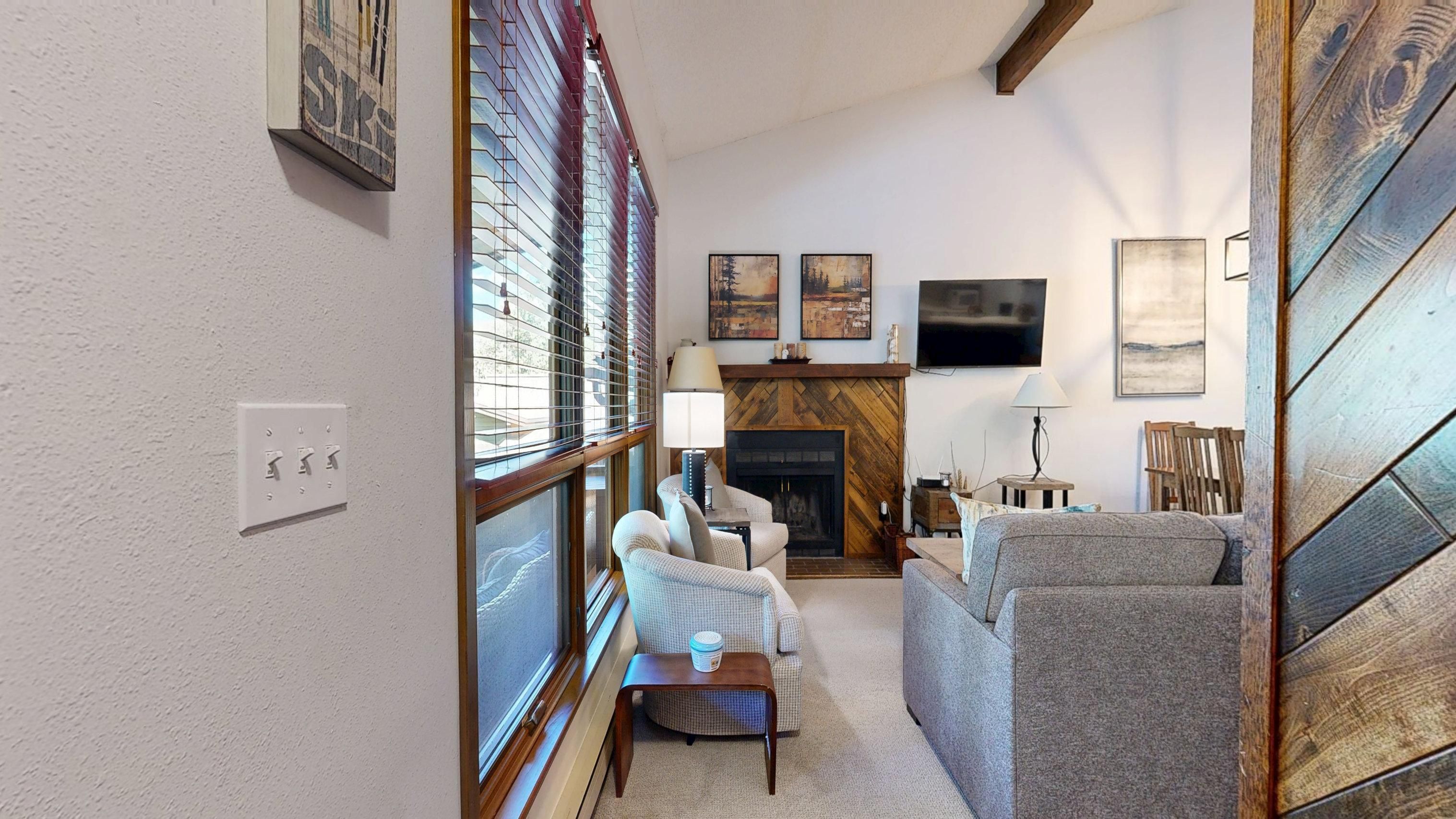 A living room with a fireplace, a television, and a window with blinds.