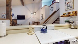Een keuken met een witte kookplaat, een blauwe waterkoker en een plafond van houten balken.