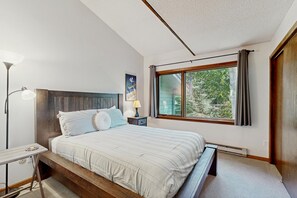 A bedroom with a bed, bedside lamp, and a window with a view of trees. - Two-story condo with wood-burning fireplace, near Beaver Creek and Vail (Avon)