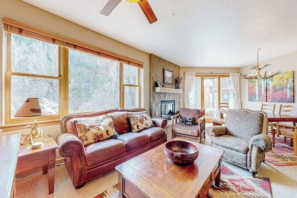 A spacious living room with a fireplace, leather sofa, and a dining area with a table and chairs. - Riverside condo with central A/C and walk-out patio at the foot of Beaver Creek (Avon)