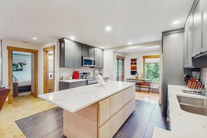 A modern kitchen with grey cabinets, a central island, and a built-in microwave. - Charming Vail Condo with Fireplace, Balcony Views, Pool & Hot Tub (Vail)