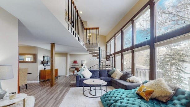 Un vaste espace de vie comprenant un escalier, de grandes fenêtres et un canapé moderne.