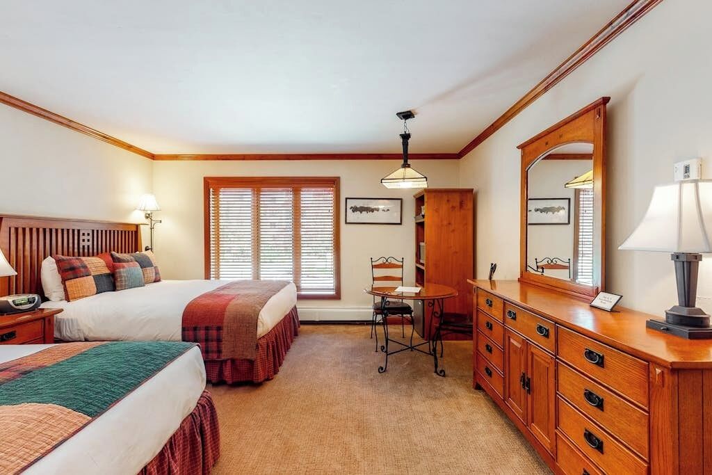 A hotel room with two beds, a wooden dresser, a desk, and a chair.