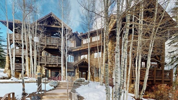 A multi-story lodge with a wooden exterior, surrounded by birch trees and snow. - Ski In ski out condo with fully stocked kitchen, wifi, and shared hot tub (Avon)
