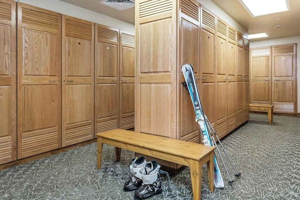 Een kleedruimte met houten kluisjes, een bankje en een paar ski's die tegen de muur staan.