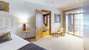 A hotel room with a bed, a bedside table with a lamp, a wooden door, a small table with chairs, and large windows. - Ski In ski out condo with fully stocked kitchen, wifi, and shared hot tub (Avon)