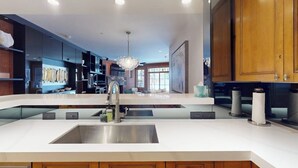 A modern kitchen with a central island, stainless steel sink, wooden cabinets, and a chandelier. - Ski In ski out condo with fully stocked kitchen, wifi, and shared hot tub (Avon)