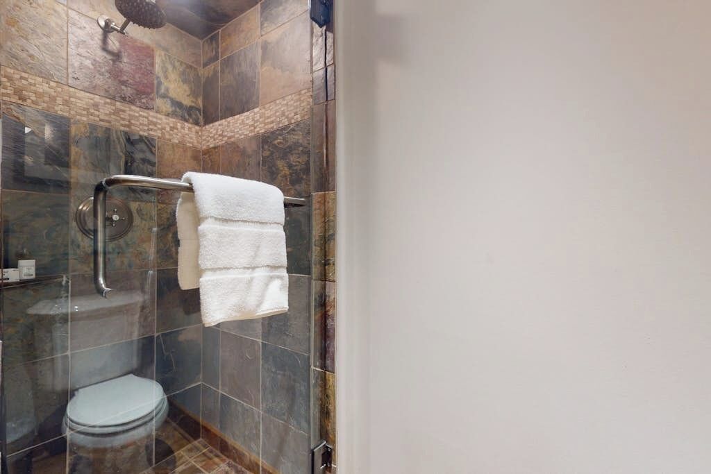A shower with a glass enclosure, a white towel, and a toilet.