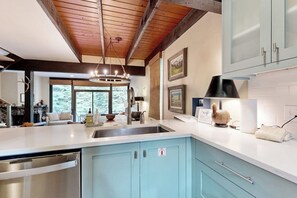 A modern kitchen with a large island, stainless steel appliances, and a view of the outdoors. - Colorful Riverfront Chalet  with Shared Pool and Hot Tub - Close to Ski Slopes (Vail)