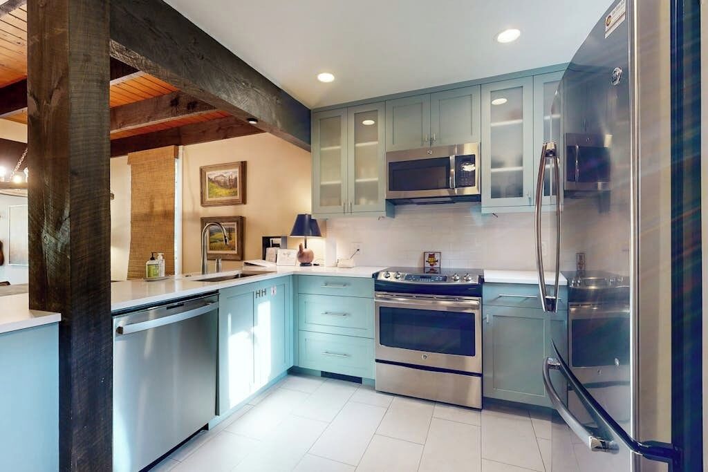 A modern kitchen with stainless steel appliances, light blue cabinets, and a wooden ceiling beam.