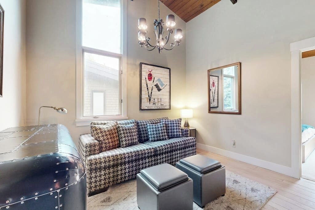 A living room with a patterned sofa, ottomans, a chandelier, and artwork on the walls.