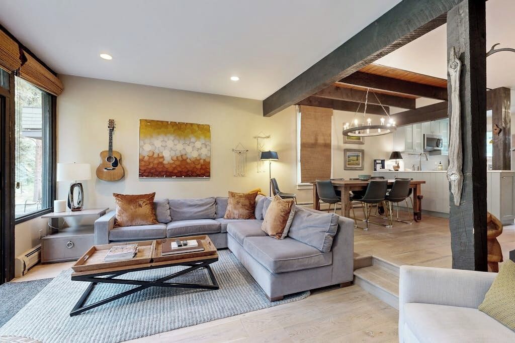 Ein modernes Wohnzimmer mit einer grauen Eckcouch, einem Couchtisch und einer Gitarre. Es gibt einen Essbereich mit Tisch und Stühlen, und im Hintergrund befindet sich eine Küche.