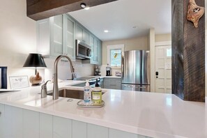 A modern kitchen with a white countertop, stainless steel appliances, and light blue cabinets. - Colorful Riverfront Chalet  with Shared Pool and Hot Tub - Close to Ski Slopes (Vail)