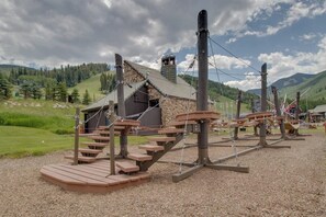Eine rustikale Holzhütte mit einem Steinhaus im Hintergrund, umgeben von einer Wiese und Bergen.