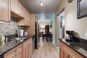 Una cocina con armarios de madera, encimera de granito, refrigerador y un comedor con mesa y sillas.