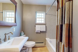 A bathroom with a sink, toilet, and bathtub, a window, and a shower curtain.